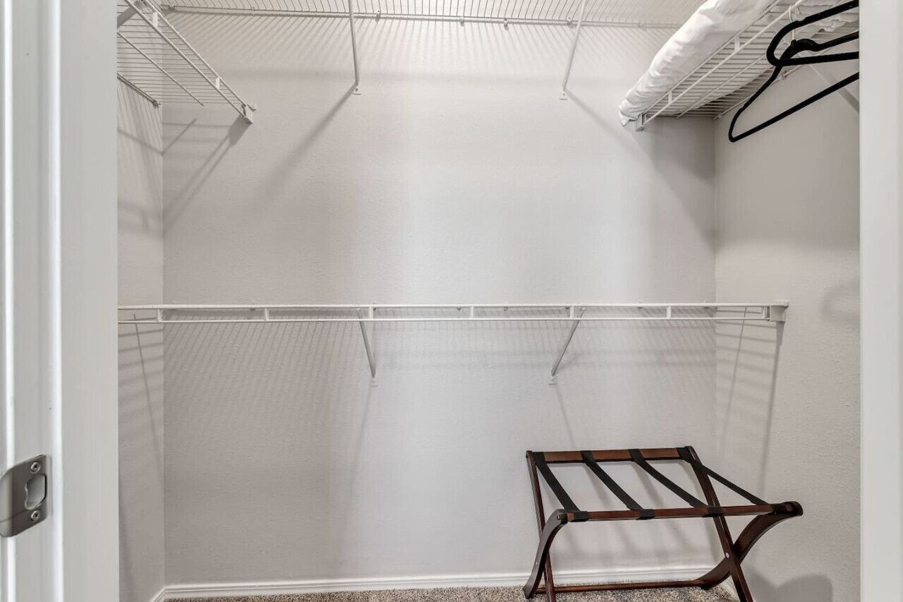 Ein begehbarer Kleiderschrank mit zwei Drahtregalen, einer hölzernen Bank und einer weißen Tür.