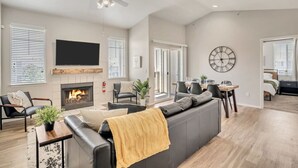 Een moderne woonkamer met een open haard, een flatscreen televisie, een plafondventilator en een eethoek met een tafel en stoelen.