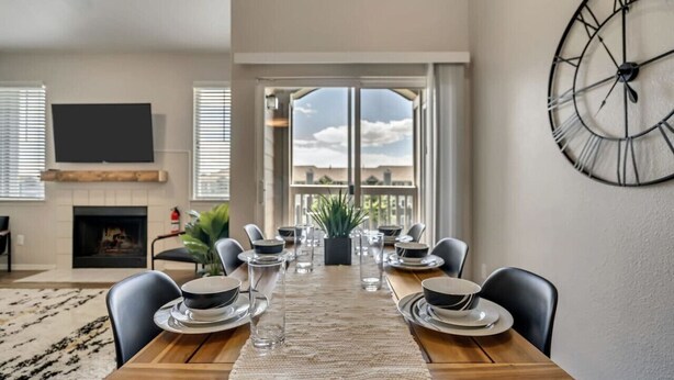 Een eethoek met een houten tafel voor vier personen, een grote wandklok en een open haard.