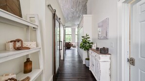 A hallway with white shelves, a wooden floor, and a white cabinet with a plant on top.