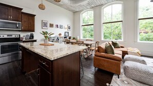 A spacious kitchen with a large island, dark wooden cabinets, and stainless steel appliances. There is a dining area with a wooden table and chairs, and a cozy seating area with a brown sofa and patterned cushions.