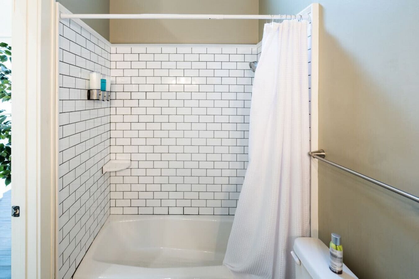 A shower area with white tiled walls, a white bathtub, and a white shower curtain.