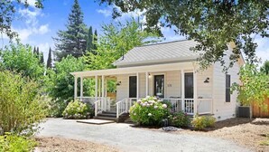 Une maison de plain-pied avec un porche, entourée de verdure et d’arbres.