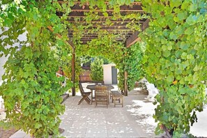Une pergola couverte de plantes grimpantes, une table en bois et des chaises, le tout dans un cadre de jardin.