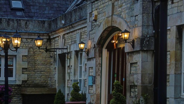 A stone building with a traditional design, featuring a central entrance with an archway, multiple windows, and outdoor seating areas with potted plants. - Normanton Park Hotel, Sure Hotel Collection by Bes (Oakham)