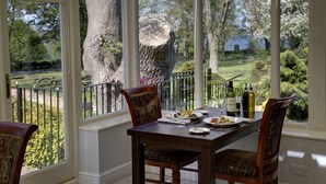 A dining area with a table set for two, a large tree outside, and a view of a garden. - Normanton Park Hotel, Sure Hotel Collection by Bes (Oakham)