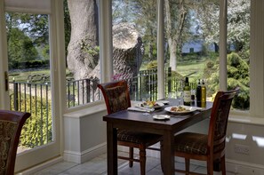 A dining area with a table set for two, a large tree outside, and a view of a garden. - Normanton Park Hotel, Sure Hotel Collection by Bes (Oakham)