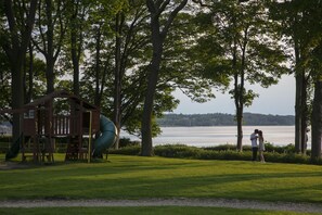 Un parque con un área de juegos, un tobogán y un lago al fondo.