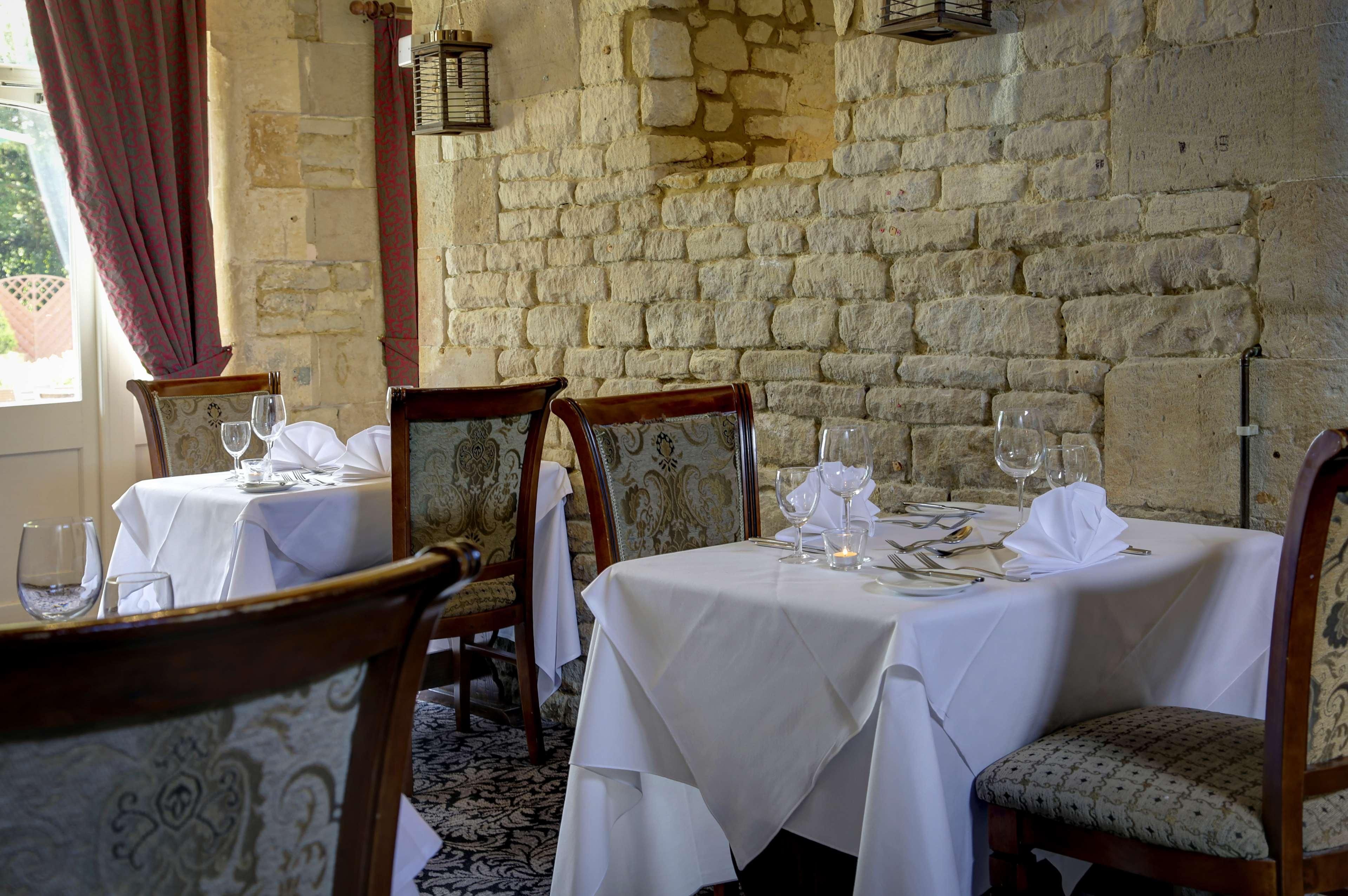 A dining area with stone walls, white tablecloths, and wooden chairs.