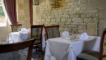 A dining area with stone walls, white tablecloths, and wooden chairs.