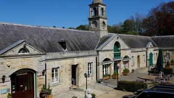 A stone building with a reception area, a clock tower, and a paved courtyard with outdoor seating.