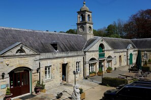 A stone building with a reception area, a clock tower, and a paved courtyard with outdoor seating.