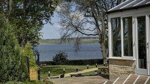 A lakeside patio with stone flooring, outdoor seating, and a view of the lake. - Normanton Park Hotel, Sure Hotel Collection by Bes (Oakham)