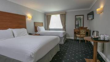 A hotel room with two beds, a desk, a chair, a coffee maker, and a TV.