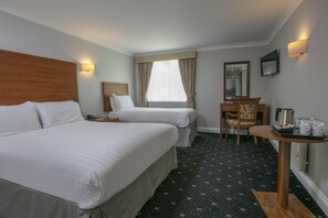 A hotel room with two beds, a desk, a chair, a coffee maker, and a TV.