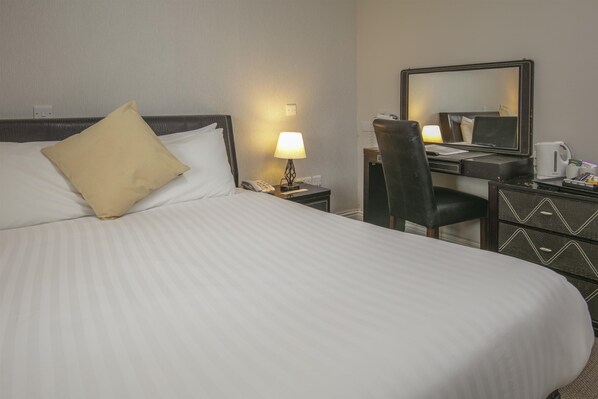 Habitación de hotel con cama, escritorio, silla, lámpara, teléfono, espejo y cafetera.
