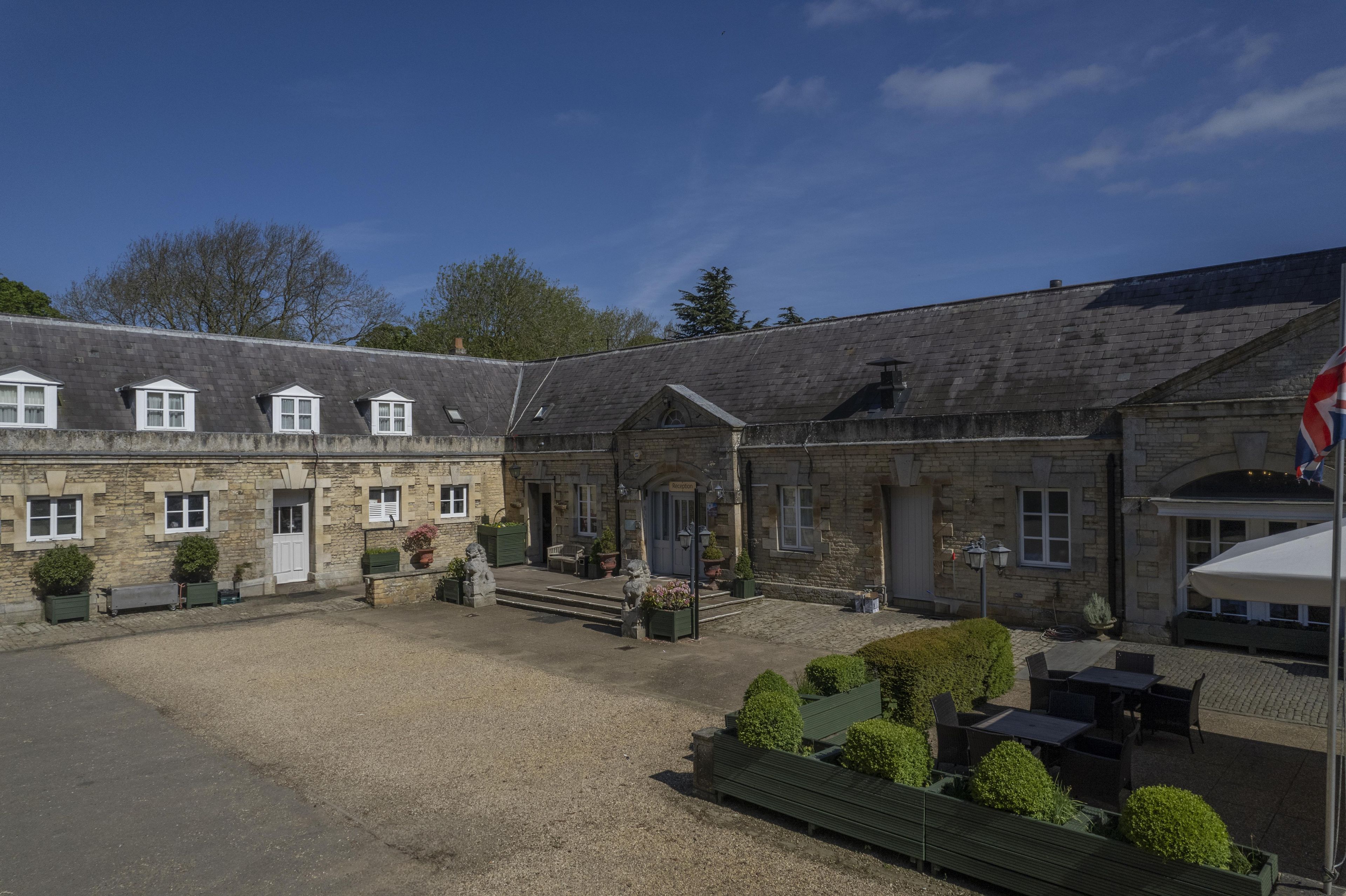 A stone building with multiple windows and a flag, a gravel courtyard, and outdoor seating.