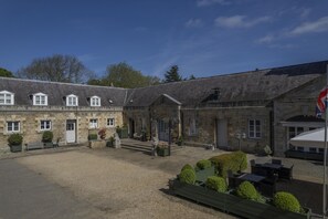 A stone building with multiple windows and a flag, a gravel courtyard, and outdoor seating.