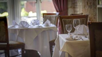 A dining table set with white tablecloths, chairs, and empty wine glasses.
