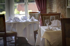 A dining table set with white tablecloths, chairs, and empty wine glasses.