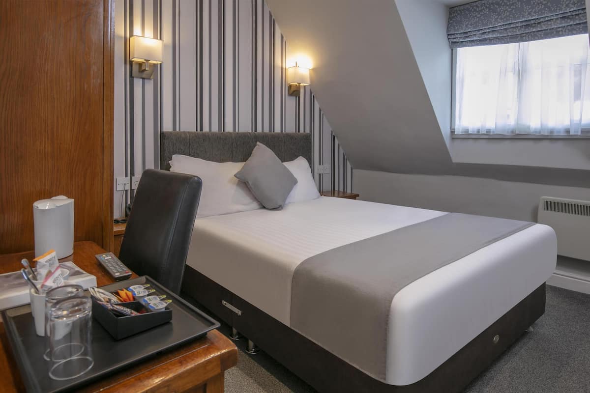 A hotel room with a bed, bedside table, lamp, and a window with curtains.
