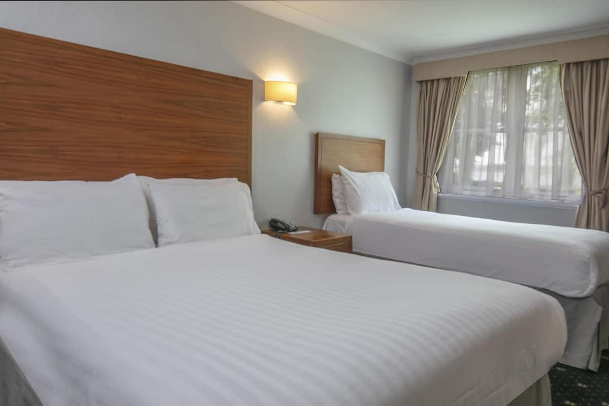 A hotel room with two beds, a wooden headboard, a bedside table with a phone, and a window with curtains.