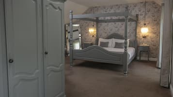 A four-poster bed with a nightstand, a dresser, and floral wallpaper.