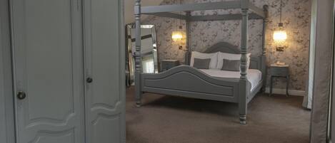 A four-poster bed with a nightstand, a dresser, and floral wallpaper.
