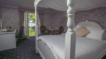 A four-poster bed with a canopy, a desk with a chair, a small table with a vase, and a balcony with a view.