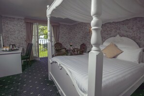 A four-poster bed with a canopy, a desk with a chair, a small table with a vase, and a balcony with a view.