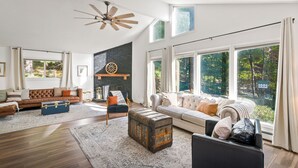 A spacious living room with a large window, a fireplace, and a ceiling fan.