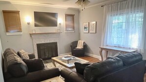 Ein Wohnzimmer mit Kamin, Ledersofas, einem Couchtisch und einem großen, an der Wand befestigten Fernseher.