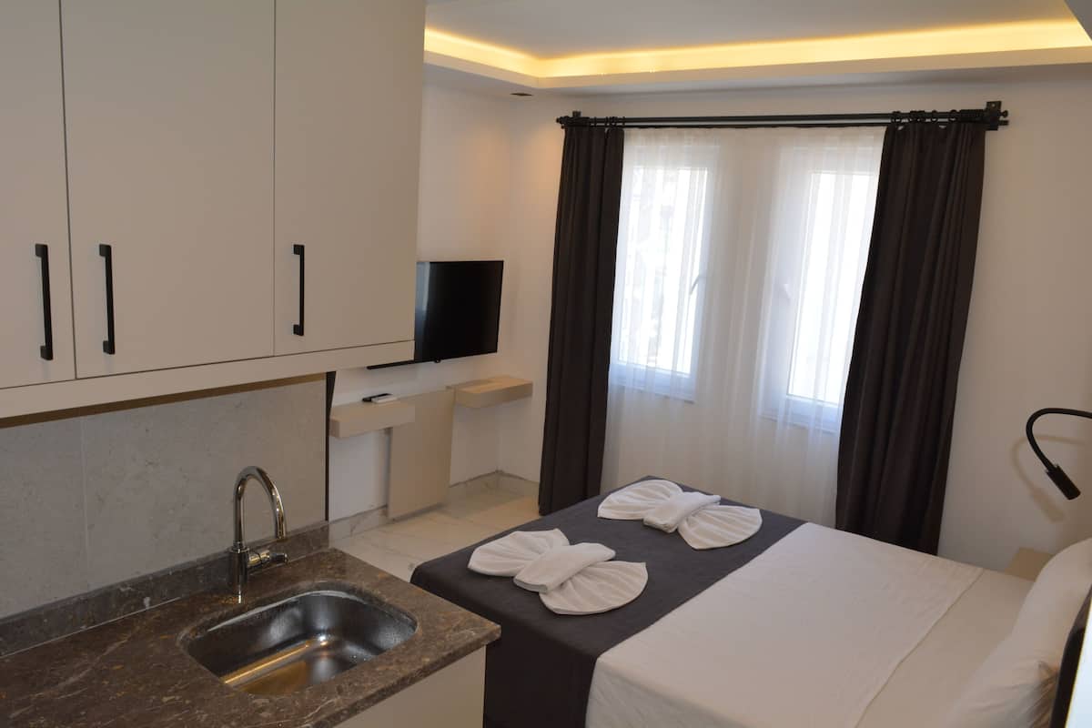 A hotel room with a bed, a TV, a sink, and a window with curtains.