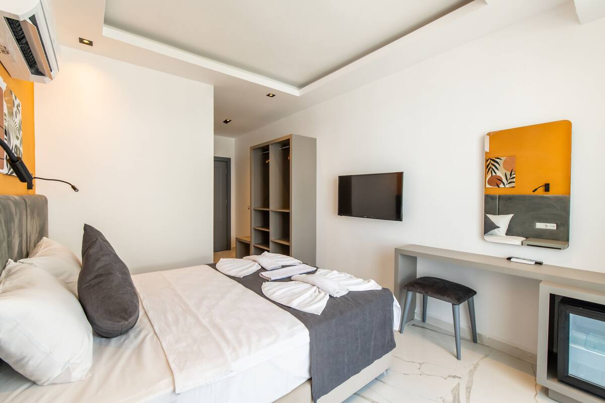 A modern hotel room with a bed, a desk, a TV, and a wardrobe.