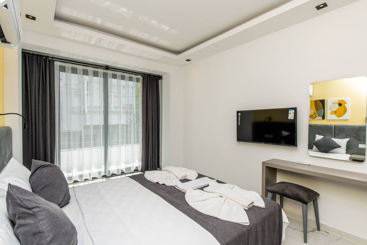 A hotel room with a bed, a desk, a TV, and a window with curtains.
