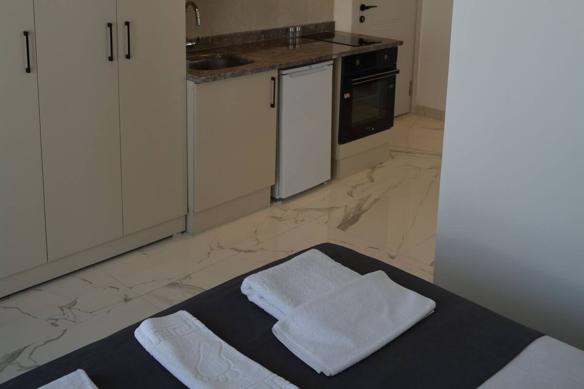 A compact hotel room with a kitchenette, a bed with towels, and a bathroom.