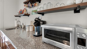 Cozinha com bancadas de granito, forno embutido, cafeteira e prateleiras com louças e copos.