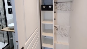 Vaatehuone, jossa on avohyllyjä, vaatetanko ja kahvallinen ovi.