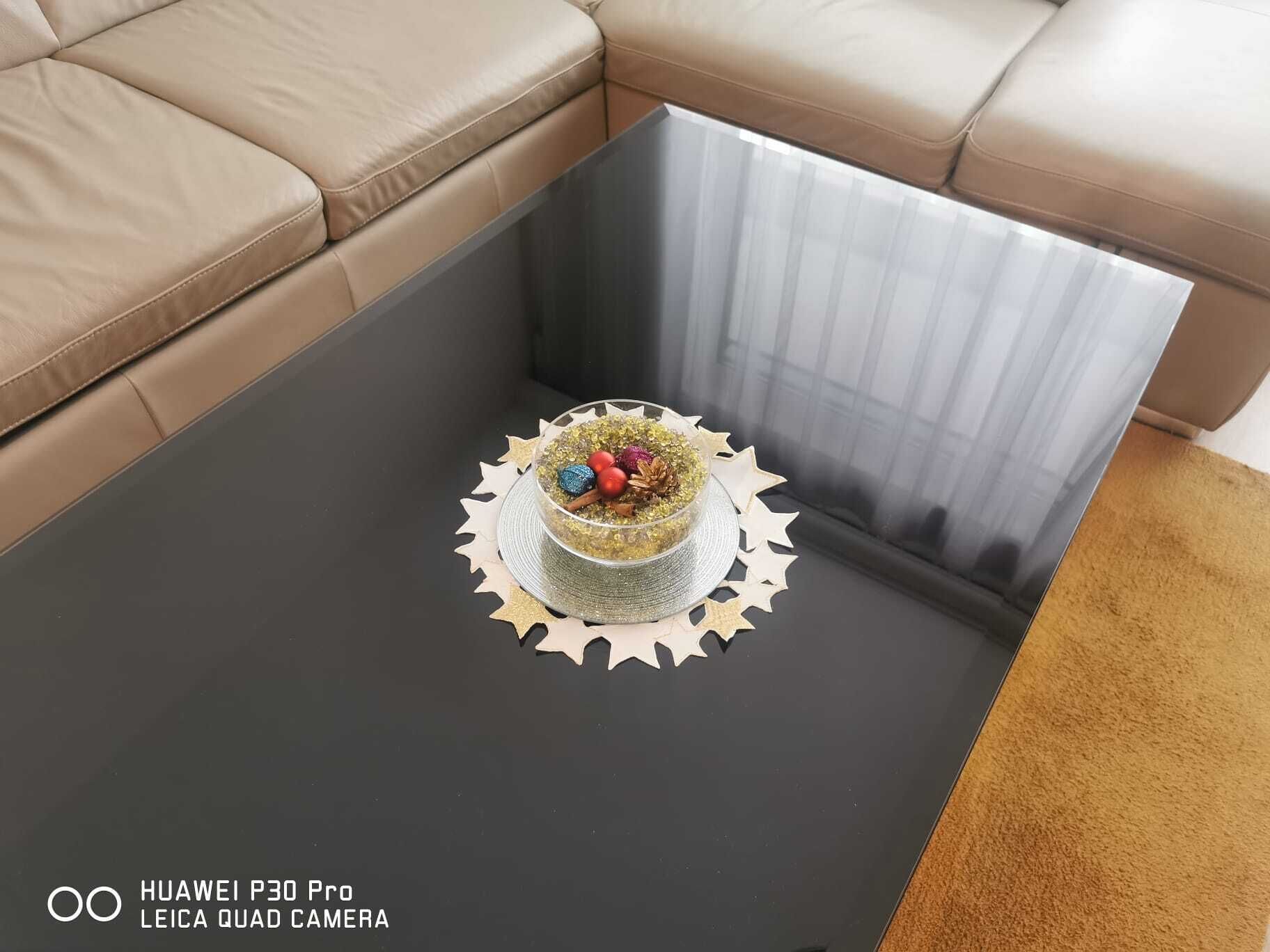 A room with a beige leather sofa, a glass coffee table with a decorative centerpiece, and a black-framed mirror.