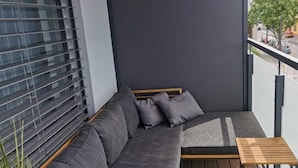 Un balcon avec un canapé gris, une petite table en bois et une vue sur la rue.