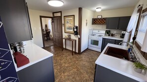 A compact kitchen with a stove, oven, and sink, a dining area with chairs, and a hallway leading to another room. - The (Veteran Owned) Hanover Hangout Guesthouse - cozy cottage w/ privacy + fun (Hanover)