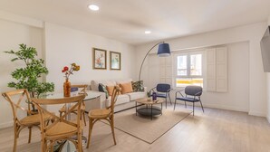 Ein modernes Wohnzimmer mit einem runden Glastisch, Holzstühlen, einer Couch und einer blauen Stehlampe.