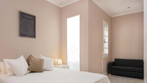 Une chambre à coucher avec un grand lit, une table de chevet avec une lampe, un canapé sombre et une fenêtre avec des stores.