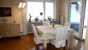 Un comedor con una mesa preparada para cuatro personas, un radiador y una ventana con cortinas.