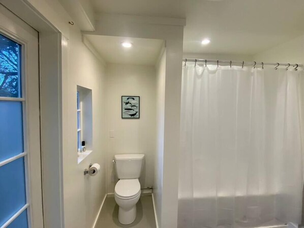 A small, white bathroom with a toilet, a framed picture on the wall, and a shower curtain.