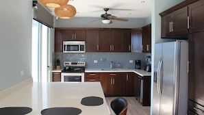Une cuisine moderne avec des meubles en bois foncé, des appareils en acier inoxydable et un îlot central blanc agrémenté de tabourets noirs.