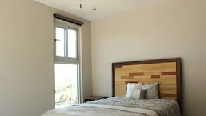 Une chambre avec une grande fenêtre, une tête de lit en bois et un lit avec une literie blanche.