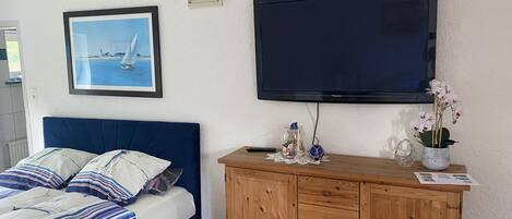 Een slaapkamer met een bed, een televisie, een kast en een lijst met een foto aan de muur.