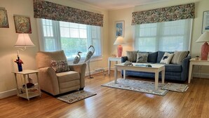 A living room with a beige armchair, a blue sofa, a white coffee table, and a patterned rug. - Cozy Cottage in quiet neighborhood not far from beaches (Marshallberg)