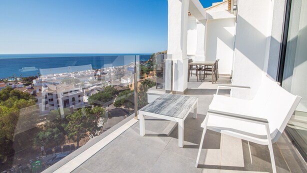 Ein Balkon mit Tisch und Stühlen, der auf eine Küstenstadt und das Meer blickt.